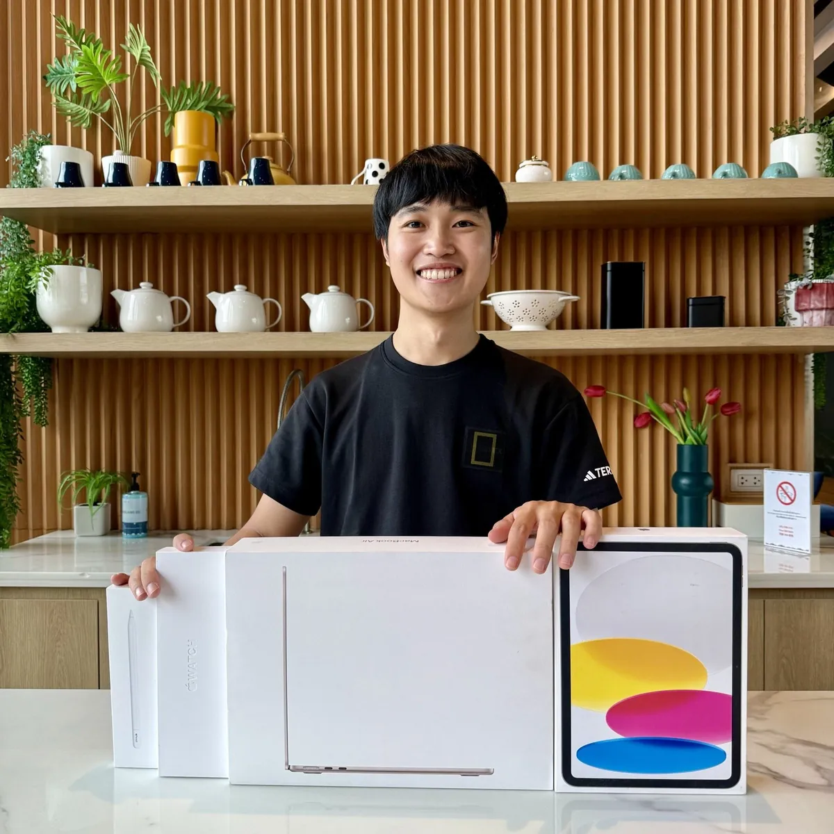 เจ้าของร้าน MU Phone ถือกล่อง MacBook Air, iPad, Apple Watch และ Apple Pencil ที่หน้าร้าน